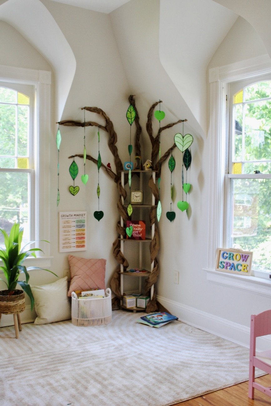 The full corner of the room, with the braided paper tree, hanging leaves and hearts, a growth mindset chart, a blush cushion, a basket of books and the Grow Space sign on the windowsill.