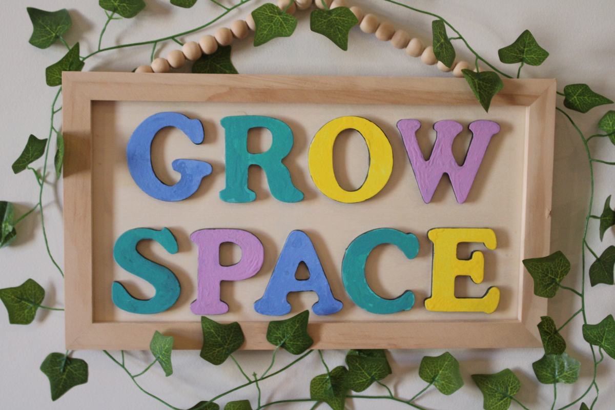 The hand painted Grow Space sign in a pale wood frame, with real ivy trailing around it.